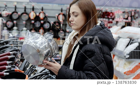Customer shopping for a new saucepan in the cookware department of a supermarket, examining stainless steel kitchenware in a housewares store Customer shopping for a new saucepan in the cookware department of a supermarket, examining stainless steel kitchenware in a housewares store 138763830