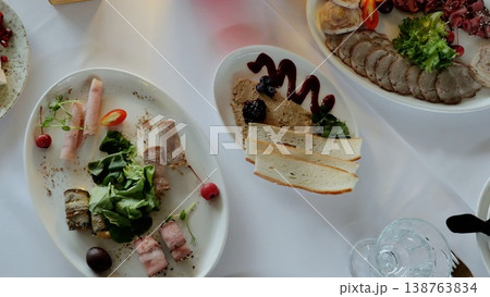 Elegant appetizer plate presenting charcuterie selection, including cured meats, pate, crisp toast points, and delicate garnishes spread across pristine white linen 138763834