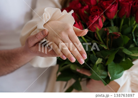 Close up of a couple holding hands with a diamond engagement ring and red roses bouquet. 138763897
