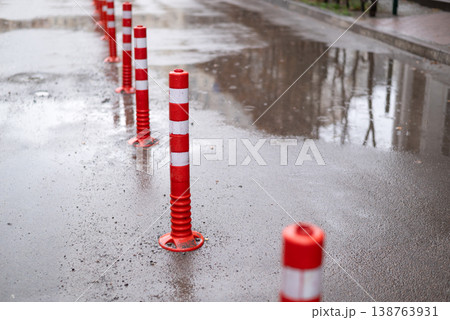 Red and white reflective traffic bollards on a wet asphalt road with puddles after rain 138763931