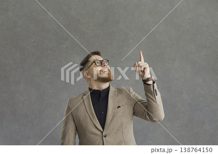 Elegant man with a happy expression looking up raises his index finger on a gray background. Elegant man with a happy expression looking up raises his index finger on a gray background. 138764150