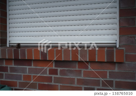 Brick wall with a window ledge and closed white shutter; a small pine cone rests on the ledge. Quiet exterior detail. Brick wall with a window ledge and closed white shutter; a small pine cone rests on the ledge. Quiet exterior detail. 138765010
