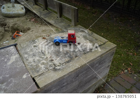 Toy truck on a weathered wooden sandbox edge, with sand and a small shovel nearby. Outdoor play scene with a tiny vehicle. Calm childhood play moment. 138765051