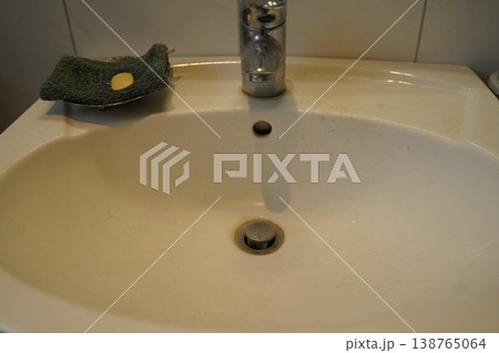 White bathroom sink with chrome faucet, drain, and green scouring pad on rim. A simple washbasin scene. 138765064