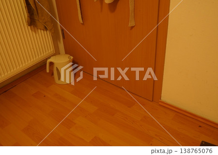 Indoor corner with wooden floor, radiator, and closed wooden door; a small plastic stool sits nearby. A quiet home hallway scene. Indoor corner with wooden floor, radiator, and closed wooden door; a small plastic stool sits nearby. A quiet home hallway scene. 138765076