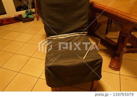 Chair with dark cover tied by string; a toothpick pierces the fabric; tiled floor and wooden table nearby indoors. Simple household scene. 138765079
