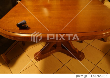 Wooden oval dining table on tiled floor, with a small hole punch on the surface and chairs around it. Indoor dining area furniture. 138765082