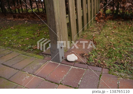 Fence post on brick walkway beside grass, with a small white stone at the base Fence post on brick walkway beside grass, with a small white stone at the base 138765110