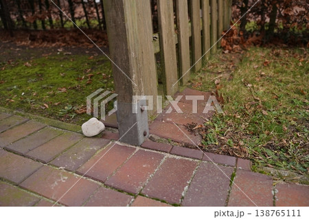 Wooden fence post base on brick paving with a white stone nearby; grass and fallen leaves beside the walkway Wooden fence post base on brick paving with a white stone nearby; grass and fallen leaves beside the walkway 138765111