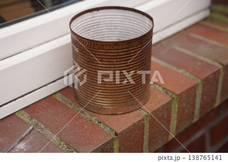 Rusty metal can on a brick ledge beside a white window frame Rusty metal can on a brick ledge beside a white window frame 138765141