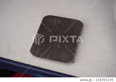Dark rectangular metal plate with rounded corners on a white tabletop, showing scratches and wear 138765144