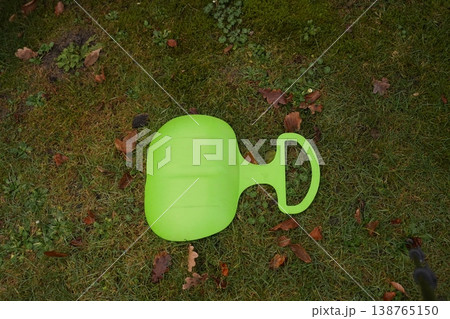 Green plastic garden sled on grass with fallen leaves Green plastic garden sled on grass with fallen leaves 138765150