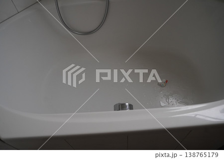 White bathtub with drain and overflow, water splash near plug, and flexible shower hose above 138765179