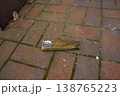 Wooden plank with a metal can lid on brick paving, outdoors near a wall 138765223