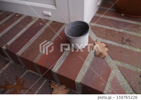 Small empty plastic flowerpot on brick step near door frame, with fallen dry leaf on patio Small empty plastic flowerpot on brick step near door frame, with fallen dry leaf on patio 138765226
