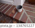 Empty plastic pot on brick step near a doorway, with fallen dry leaf on the ground 138765227