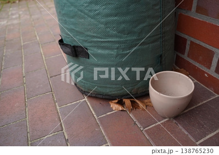 Green padded cylinder with strap on brick pavement beside a brick wall, with a ceramic bowl and dry leaves on the ground 138765230