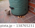 Green fabric container on tiled floor near brick wall, with beige cup and dry leaf beside it 138765231