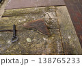 Rusty metal shard and a key lying on a weathered wooden tabletop near brick paving 138765233