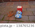 Dirty red and blue toy truck on brick pavement with a fallen brown leaf nearby 138765236