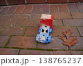 Small toy vehicle on brick pavement beside a dry leaf; red and blue plastic, worn and dirty, outdoors 138765237