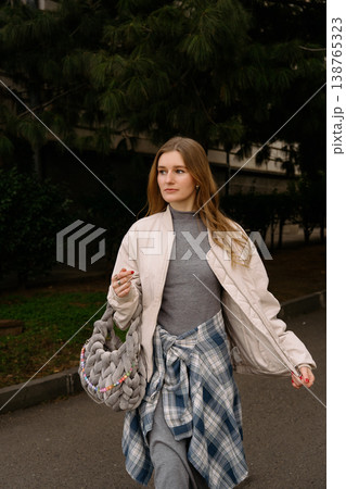 Young woman walks down a city street while holding a bag in the daytime Young woman walks down a city street while holding a bag in the daytime 138765323