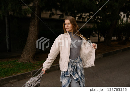 Young woman walks down street holding bag in city during daytime in casual clothing Young woman walks down street holding bag in city during daytime in casual clothing 138765326