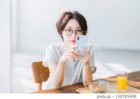 スマホを見ながら朝食を食べる女性 138765406