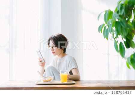 スマホを見ながら朝食を食べる女性 138765437