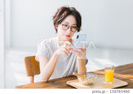 スマホを見ながら朝食を食べる女性 スマホを見ながら朝食を食べる女性 138765460
