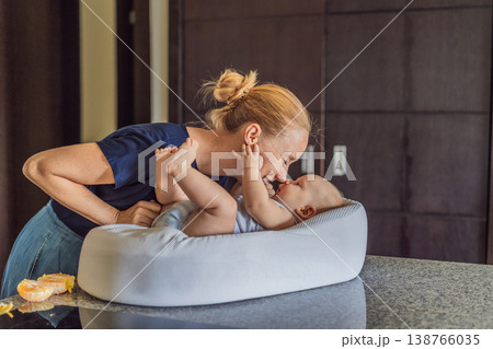 Mother talking to baby lying in cozy lounger on kitchen table while cooking at home. Caring mom interacting with infant during daily routine. Parenting, multitasking and family life concept Mother talking to baby lying in cozy lounger on kitchen table while cooking at home. Caring mom interacting with infant during daily routine. Parenting, multitasking and family life concept 138766035
