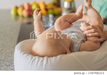 Mother and son preparing smoothie in kitchen while baby lies in cozy lounger on table watching. Family cooking together, healthy lifestyle, parenting, sibling bonding and everyday life concept Mother and son preparing smoothie in kitchen while baby lies in cozy lounger on table watching. Family cooking together, healthy lifestyle, parenting, sibling bonding and everyday life concept 138766222