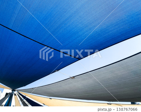 Colorful shade sails in outdoor location to provide from sun, closeup. Multiple sails in different shades of blue and gray, comfortable spot. Bright sunlight shining through gaps between sails Colorful shade sails in outdoor location to provide from sun, closeup. Multiple sails in different shades of blue and gray, comfortable spot. Bright sunlight shining through gaps between sails 138767066