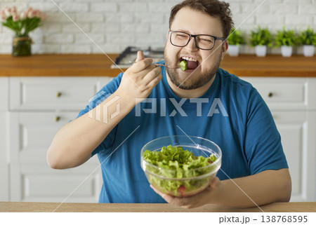 Plus-size man enjoying fresh green salad at home kitchen, healthy diet concept 138768595