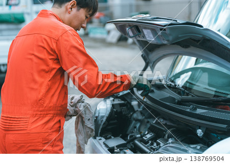 レベルゲージを抜いてオイル状態を確認する自動車整備士 138769504