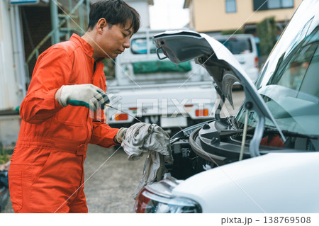 車のボンネットを開いてからオイルレベルゲージを抜き、付着しているエンジンオイルをウエスで一度拭き取る 138769508