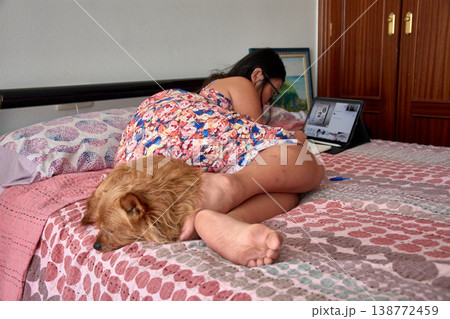 Young woman lying in bed looking at her tablet next to her sleeping dog during a relaxing afternoon at home Young woman lying in bed looking at her tablet next to her sleeping dog during a relaxing afternoon at home 138772459