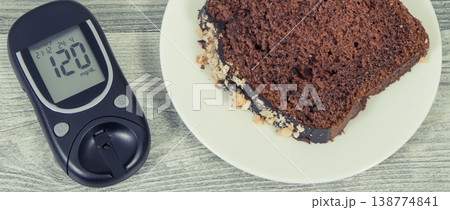 Glucose meter with high result sugar level and sweet chocolate cake. Nutrition during diabetes Glucose meter with high result sugar level and sweet chocolate cake. Nutrition during diabetes 138774841