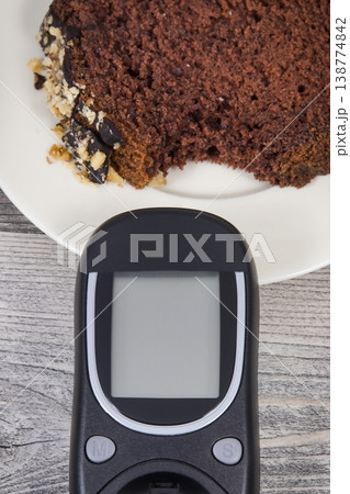 Glucometer for measuring sugar level and sweet chocolate cake. Nutrition during diabetes Glucometer for measuring sugar level and sweet chocolate cake. Nutrition during diabetes 138774842