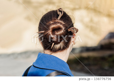 Woman with neat hair bun secured by wooden hairpin wearing a blue coat photographed from behind Woman with neat hair bun secured by wooden hairpin wearing a blue coat photographed from behind 138776756
