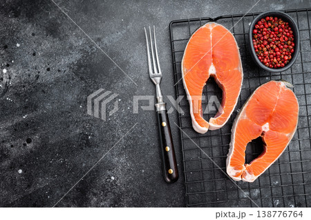 Raw sockeye salmon steaks also known as coho on metal rack with pepper and fork, dark stone background with copy space Raw sockeye salmon steaks also known as coho on metal rack with pepper and fork, dark stone background with copy space 138776764