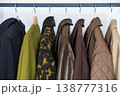 A row of autumn, winter and spring coats in earthy tones hanging on a sleek clothing rack.  138777316