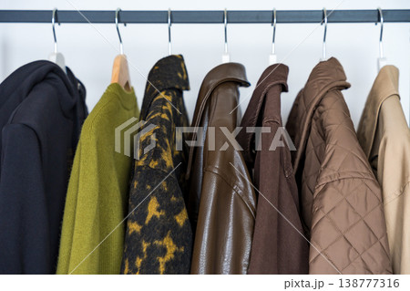 A row of autumn, winter and spring coats in earthy tones hanging on a sleek clothing rack.  138777316