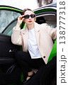 Stylish woman in sunglasses stepping out of a green car in an elegant beige coat 138777318