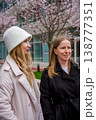 Two caucasian women dressed in stylish coats are smiling and walking outdoors in an urban area  138777351
