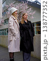 Two caucasian women dressed in stylish coats are smiling and walking outdoors in an urban area. 138777352