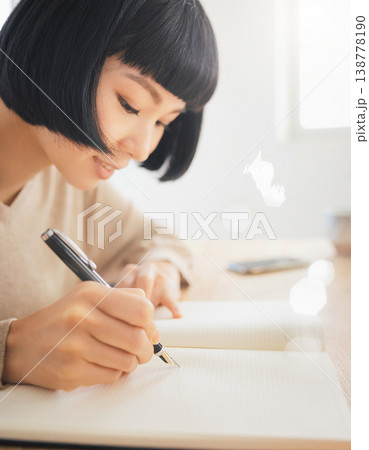 ノートに万年筆で書く女性の手元と横顔 138778190