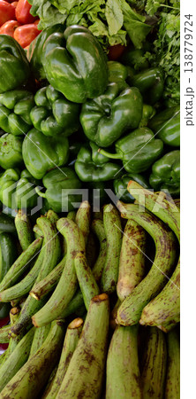 Ridge gourd stacked with green bell peppers and fresh vegetables in market showing organic produce display Ridge gourd stacked with green bell peppers and fresh vegetables in market showing organic produce display 138779724