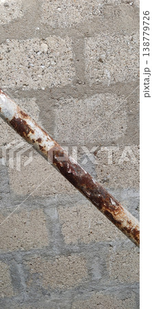 Rusty metal pipe against rough concrete wall showing corrosion and weather damage Rusty metal pipe against rough concrete wall showing corrosion and weather damage 138779726