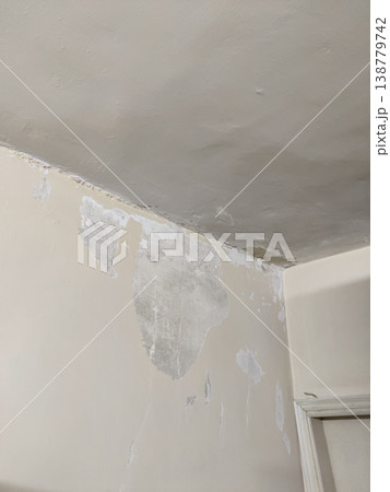 Wall corner near ceiling with peeling paint and exposed plaster caused by water seepage damage Wall corner near ceiling with peeling paint and exposed plaster caused by water seepage damage 138779742
